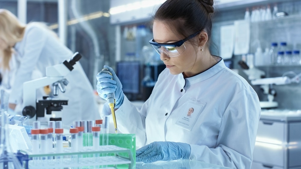 Female Research Scientist Uses Micropipette Filling Test Tubes in a Big Modern Laboratory. In the Background Scientists are Working.